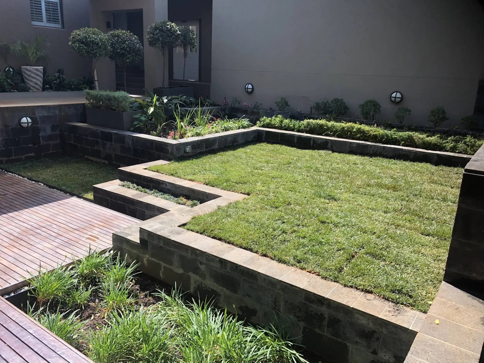 Terraced new lawn with charcoal retaining walls and timber deck walkway, installed by Turfex in Kyalami